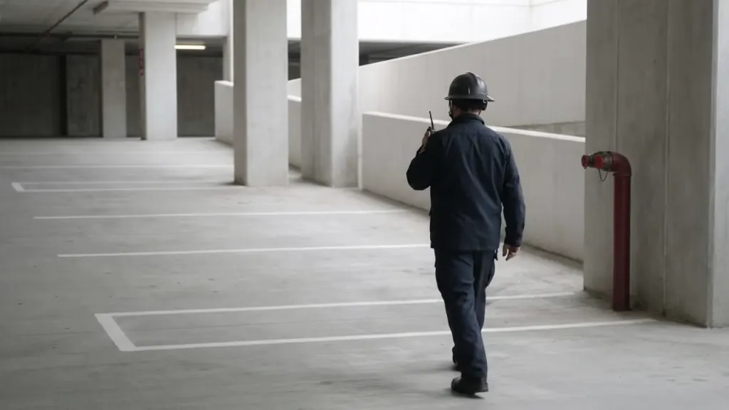A responder in dark work clothes walks through a parking garage with a radio at his shoulder.